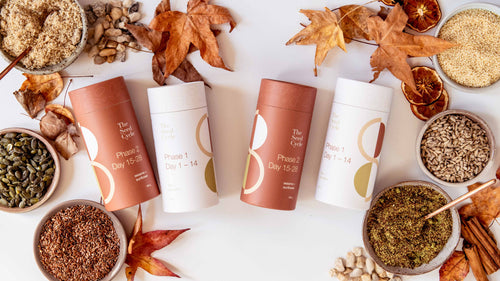 Flat lay of seed cycling blends and ingredients styled with autumn leaves—showing jars of flax, pumpkin, sesame, and sunflower seeds alongside The Seed Cycle packaging in warm seasonal tones.