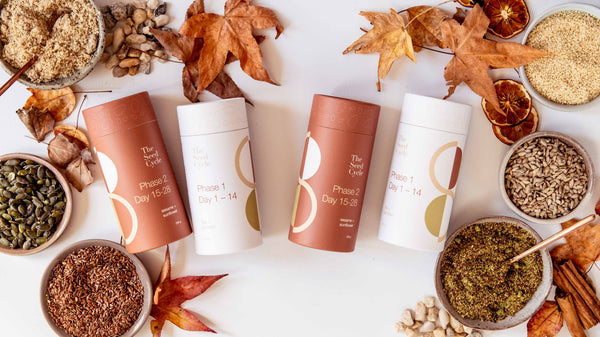 Flat lay of seed cycling blends and ingredients styled with autumn leaves—showing jars of flax, pumpkin, sesame, and sunflower seeds alongside The Seed Cycle packaging in warm seasonal tones.