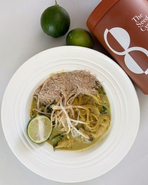 Gourmet green curry noodle bowl with "The Seed Cycle" terracotta canister and fresh limes
