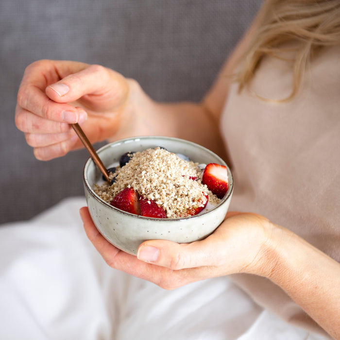 Woman holding a bowl of oats topped with The Seed Cycle blend